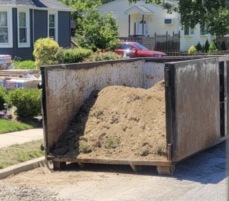 dumpster on a residential street filled with dirt