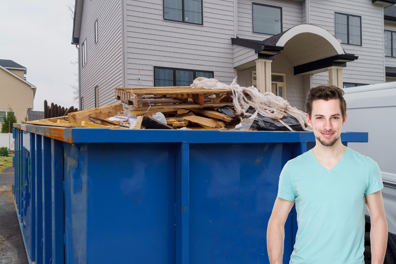 Man in front of a dumpsters being filled with garbage in front of his house