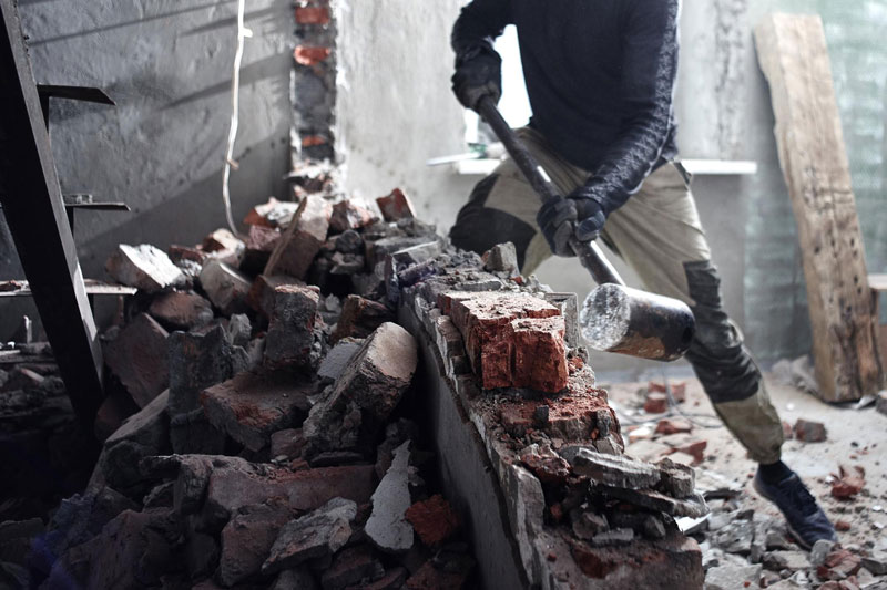 A man handyman breaks a brick wall with a hammer, builds and repairs his house after demolition