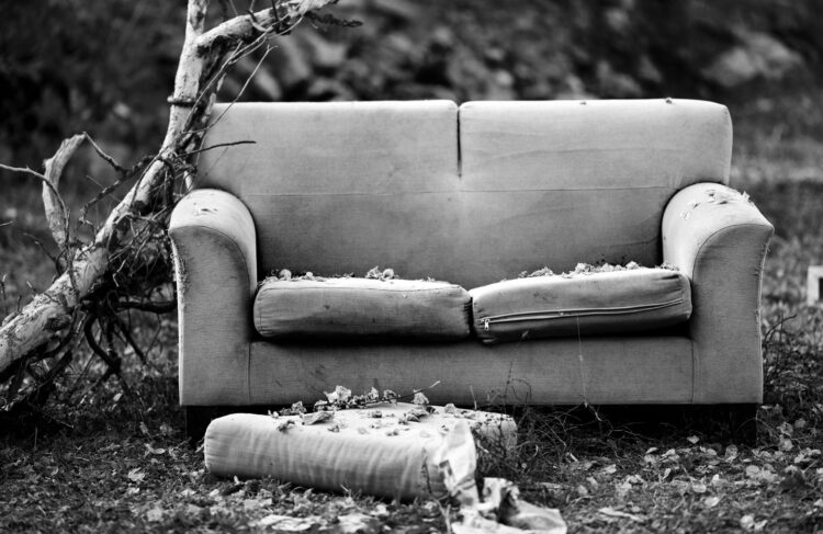 old couch on the front lawn covered in leaves, black and white photo.
